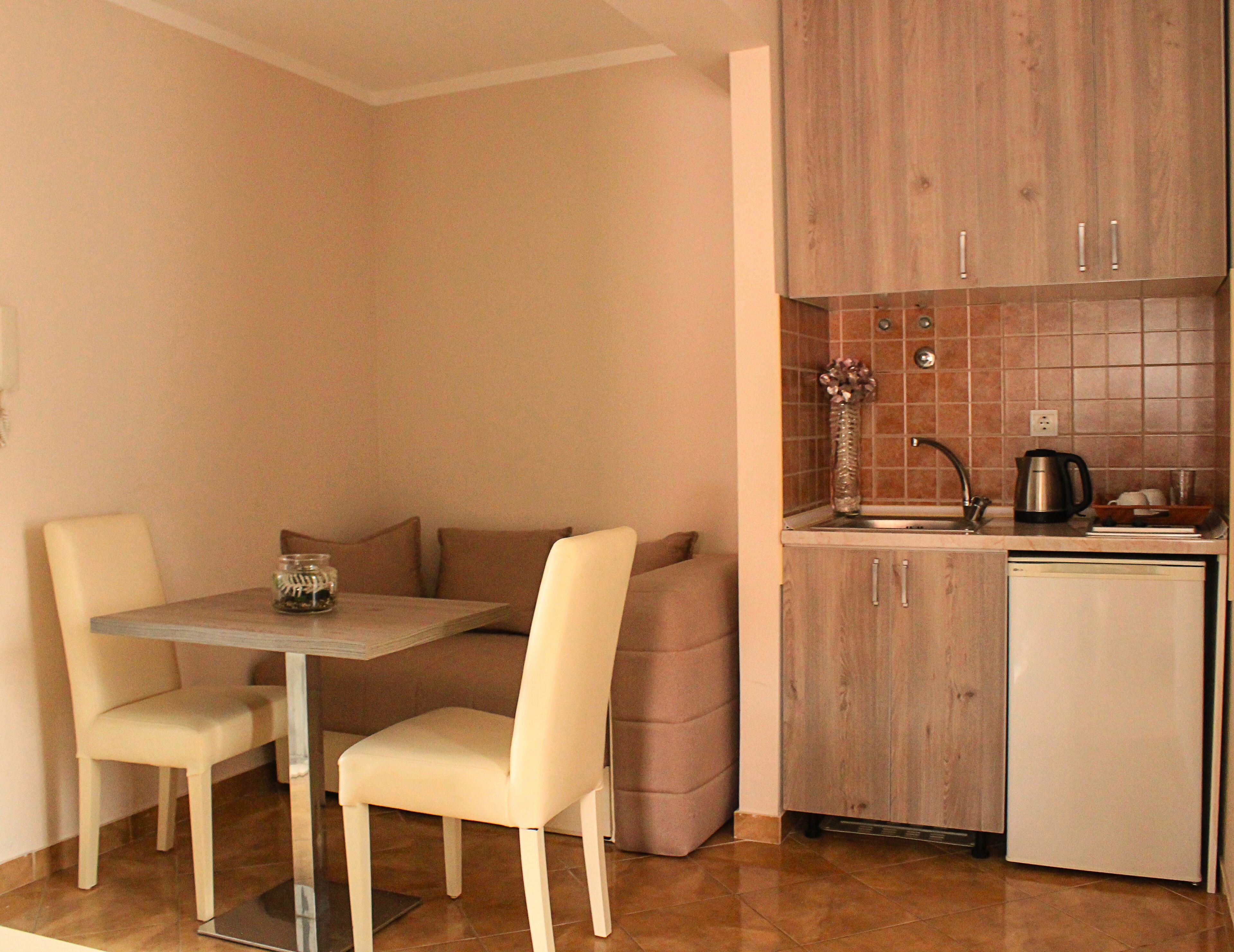 A compact kitchen with a dining area, featuring a small table, two chairs, a sink, and a refrigerator.