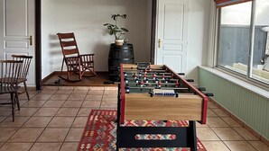 A room with a foosball table, two rocking chairs, a plant, and a window with a view. - Matsya Hostel (Anglet)