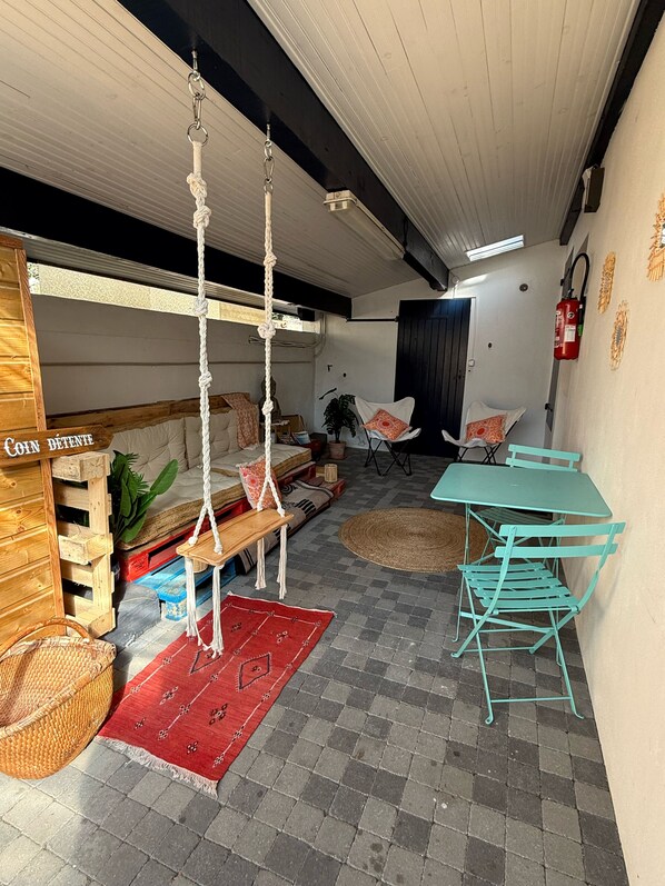 A cozy room with a swing, a small table, chairs, and a red rug. - Matsya Hostel (Anglet)