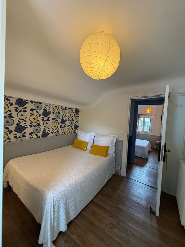 A bedroom with a bed, a patterned wall, a ceiling light, and a door leading to another room. - Matsya Hostel (Anglet)