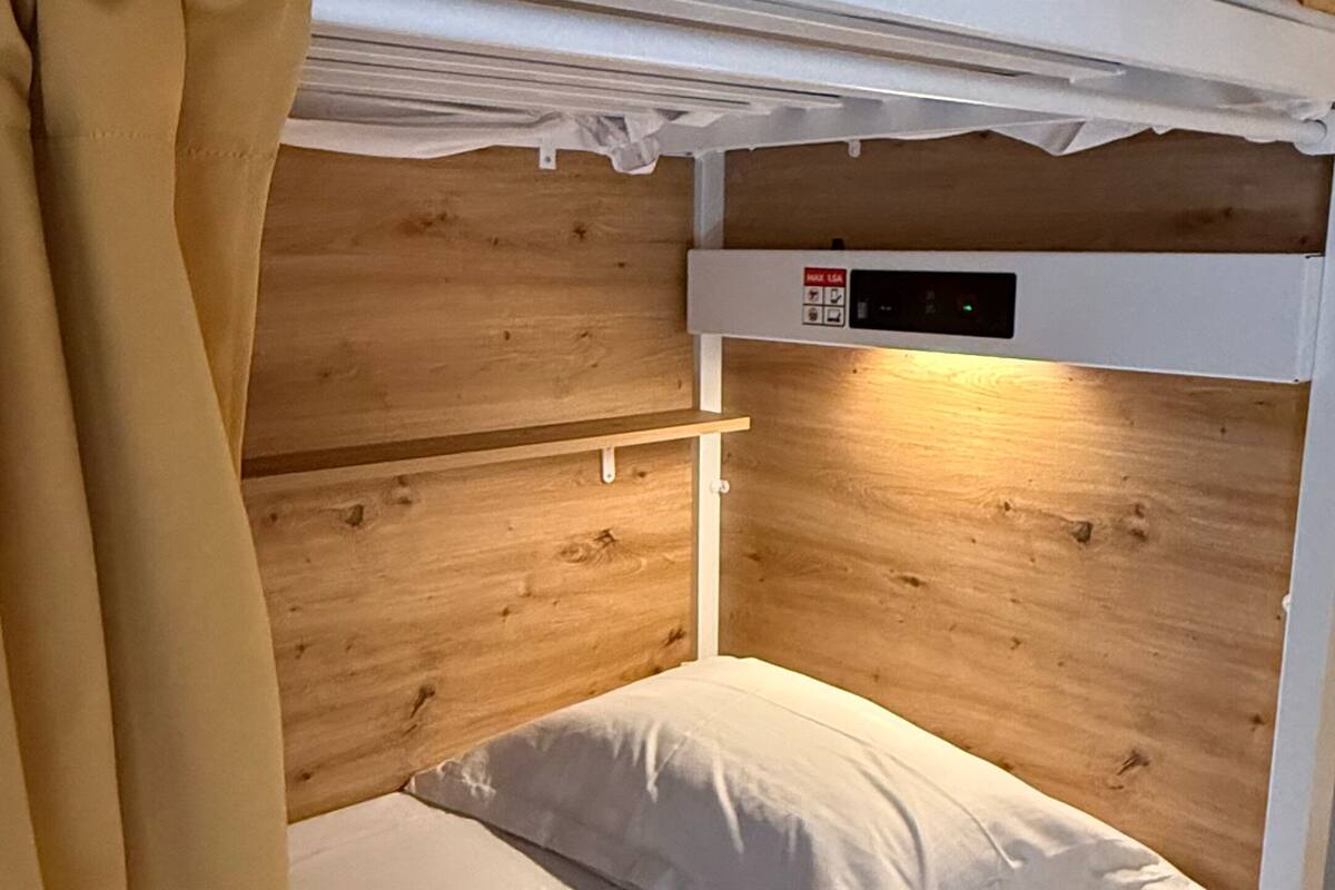 Una cama litera con cabecera de madera, colchón blanco y panel de control lateral.