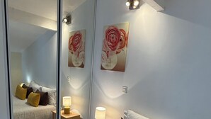 A modern bedroom with a large bed, bedside lamps, a mirror, and two wall-mounted paintings. - Matsya Hostel (Anglet)