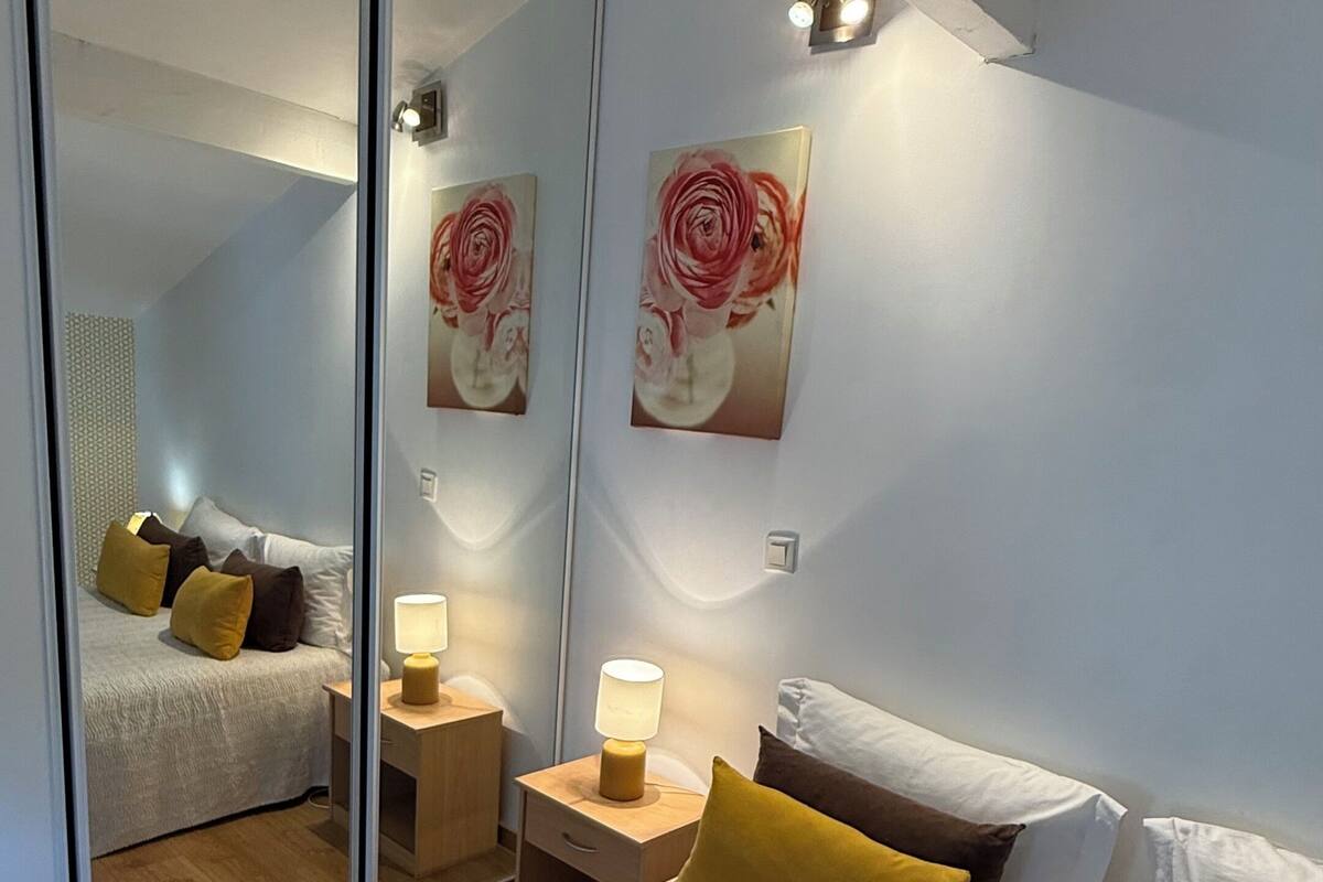 Un dormitorio moderno con una cama grande, lámparas de noche, un espejo y dos cuadros colgados en la pared.