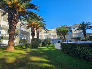 Un patio de hotel con palmeras, un césped cuidado y un edificio de varios pisos con balcones.