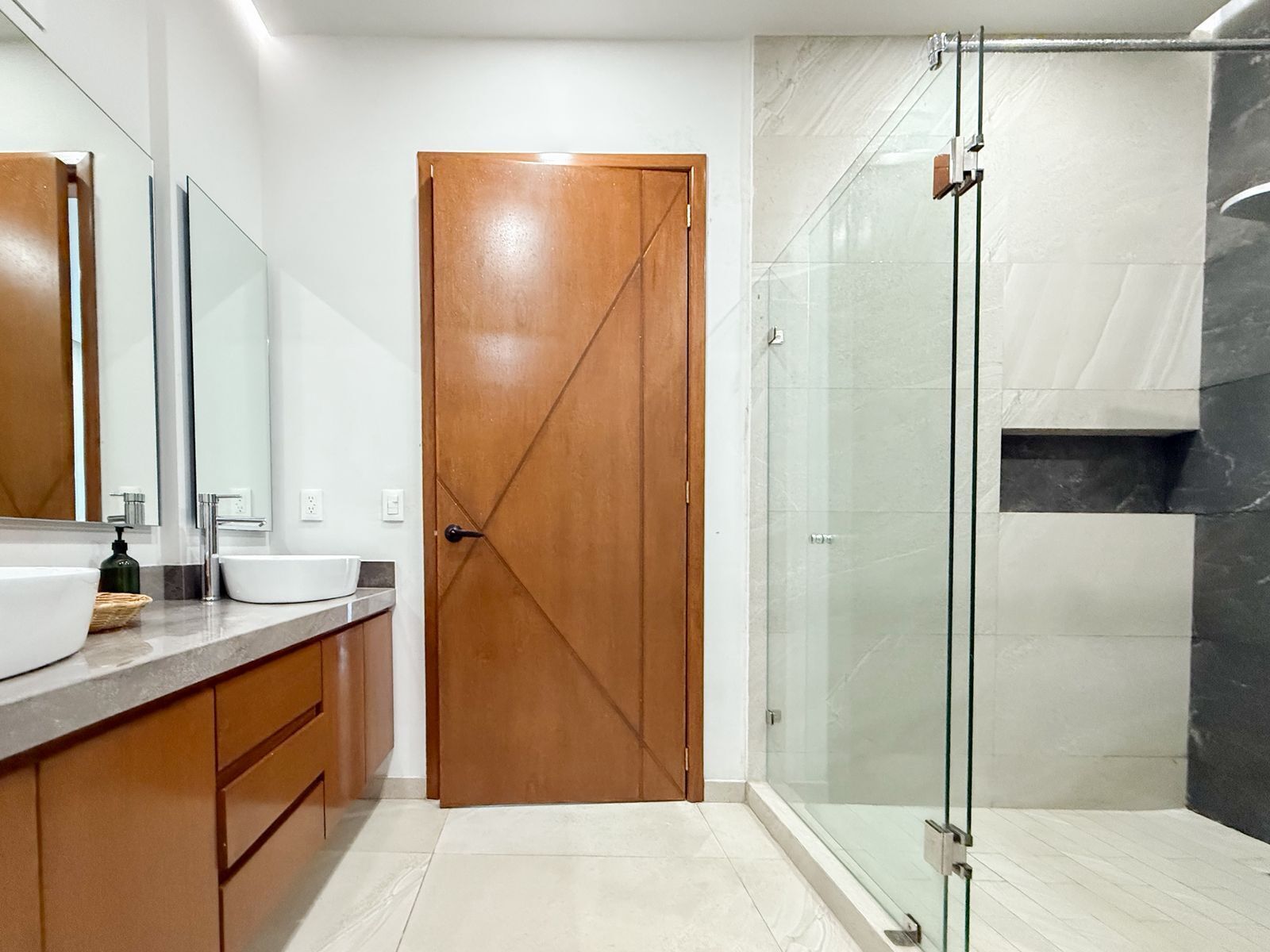 Un baño moderno con puerta de madera, cabina de ducha de vidrio y un espejo grande.