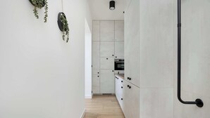 Una cocina estrecha con armarios de colores claros, suelo de madera y plantas colgantes.