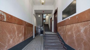 Un pasillo con suelo de mármol, una escalera, una araña y una placa en la pared.