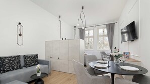 Una sala de estar moderna con un sofá gris, una mesa de comedor para cuatro comensales y un televisor montado en la pared.