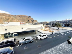 A parking area with multiple cars, a building with a flat roof, and a mountainous backdrop. - Casa Melinda  - Playa de Mogan (Lomo Quiebre)