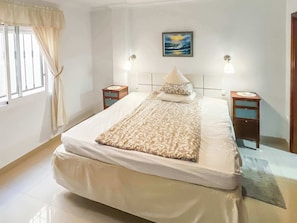 A bedroom with a bed, two bedside tables, a nightstand, a window with curtains, and a painting on the wall. - Casa Melinda  - Playa de Mogan (Lomo Quiebre)