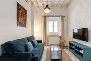 A living room with a sofa, a TV, a lamp, and a window. - Casa San Vicente Olehousing 1 (Sevilla)