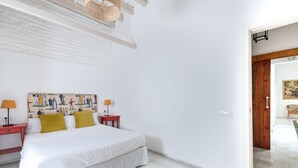 Un dormitorio con una cama, dos mesitas de noche, una lámpara de pared y una puerta que da a otra habitación.