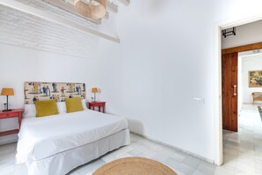 A bedroom with a bed, two bedside tables, a wall-mounted lamp, and a door leading to another room. - Casa San Vicente Olehousing 1 (Sevilla)