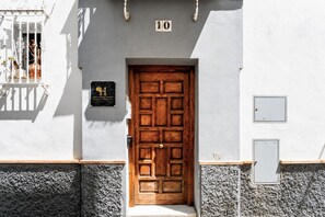 Eine Holztür mit einem Schild darüber, ein Balkon mit Pflanzen und die Zahl 10 an der Wand.