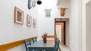 Un pasillo con una mesa de madera, sillas, una lámpara colgante, cuadros enmarcados y una cesta tejida.