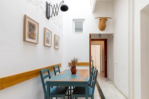 A hallway with a wooden-framed table, chairs, a hanging light fixture, framed pictures, and a woven basket. - Casa San Vicente Olehousing 1 (Sevilla)