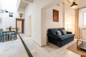 Ein modernes Wohnzimmer mit einem dunkelblauen Sofa, einem Essbereich mit grünen Stühlen und einer im Hintergrund sichtbaren Küche.
