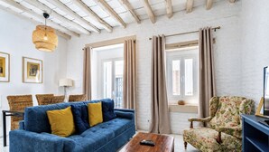 Un soggiorno con un divano blu, un tavolino in legno, una poltrona con motivi floreali, sedie in vimini e una lampada a sospensione.