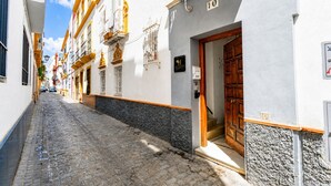 A narrow cobblestone street flanked by buildings with balconies and a wooden door. - Casa San Vicente Olehousing 3 (Sevilla)