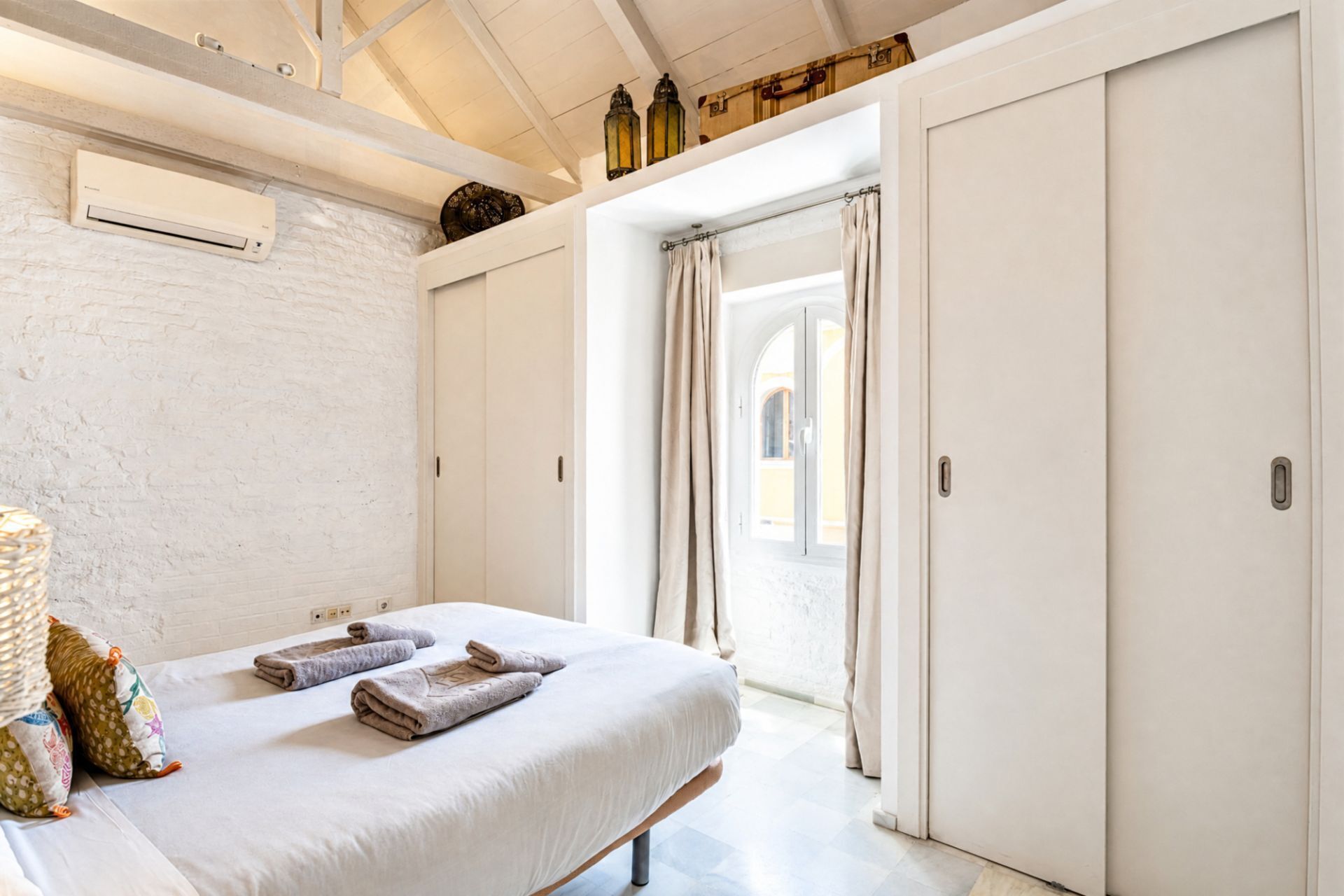 Een slaapkamer met een bed, twee nachtkastjes, een witte muur, een raam met gordijnen en een deur.