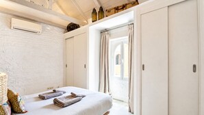 A bedroom with a bed, two bedside tables, a white wall, a window with curtains, and a door. - Casa San Vicente Olehousing 3 (Sevilla)