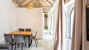 A dining area with a wooden table and chairs, a hanging light fixture, and a view through large windows. - Casa San Vicente Olehousing 3 (Sevilla)