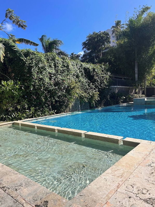 A clear swimming pool with a stone border, surrounded by lush greenery and a building in the background. - See you at the Sea, Lovely Condo for a Great Getaway in Las Terrenas (Las Terrenas)
