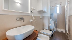 Une salle de bain moderne avec un grand lavabo ovale, des toilettes, un espace douche et un miroir.