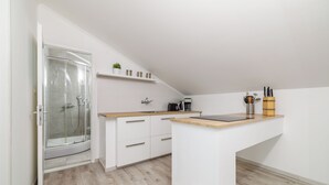 Moderni keittiö, jossa on kiinteä keittiösaareke, lasinen suihkuseinä ja valkoiset sisustuselementit.