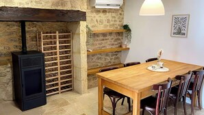 A rustic dining area with a wooden table, chairs, a black wood stove, and a stone wall. - Villa sleeps 10 with heated pool & jacuzzi and breathtaking views (Coux and Bigaroque-Mouzens)