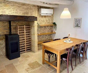 Un coin repas rustique avec une table en bois, des chaises, un poêle en bois noir et un mur en pierre.