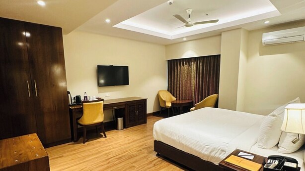 A hotel room with a bed, desk, chair, and a flat-screen TV. - Park Selections (Bhubaneshwar)