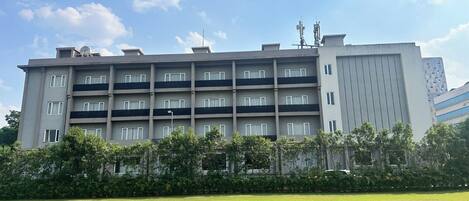 A multi-story building with balconies, a flat roof, and a large grassy area in front.