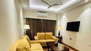 A living room with a sofa set, a coffee table, a ceiling fan, an air conditioning unit, a television, and a lamp. - Park Selections (Bhubaneshwar)