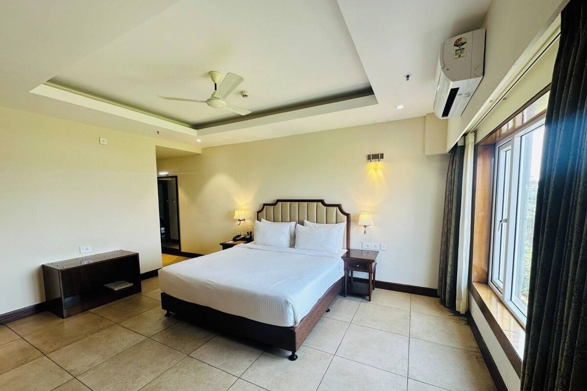 Habitación de hotel con una cama grande, dos mesitas de noche, un ventilador de techo y una ventana con cortinas.