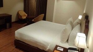 A hotel room with a bed, a desk, two chairs, a lamp, an air conditioning unit, and a telephone. - Park Selections (Bhubaneshwar)