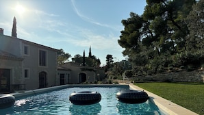 Une piscine avec des bouées gonflables, un mur en pierre et un bâtiment doté de fenêtres en arc de cercle.