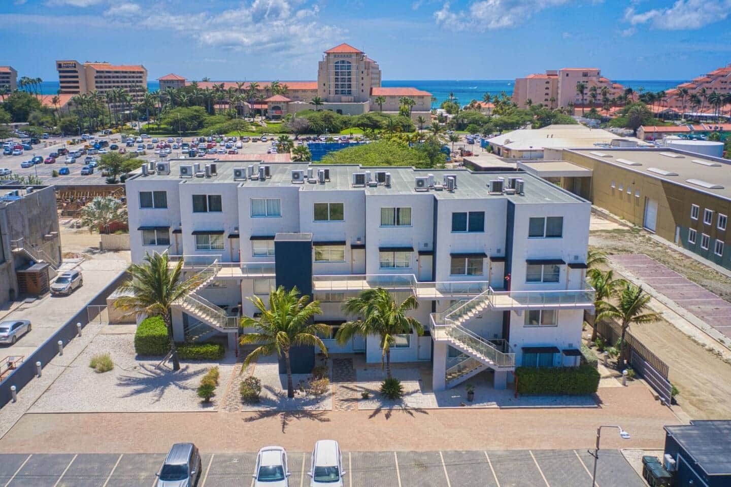 A multi-story hotel with a central courtyard, parking lot, and a view of the beach and ocean.