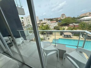 Un balcon avec une piscine, des fauteuils en osier blancs et une vue sur les bâtiments environnants.