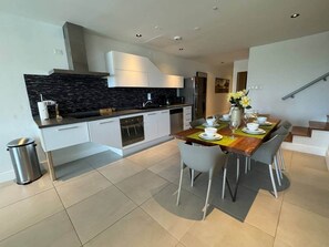 Une cuisine moderne avec des meubles blancs, un plan de travail noir et un coin repas comprenant une table et des chaises en bois.