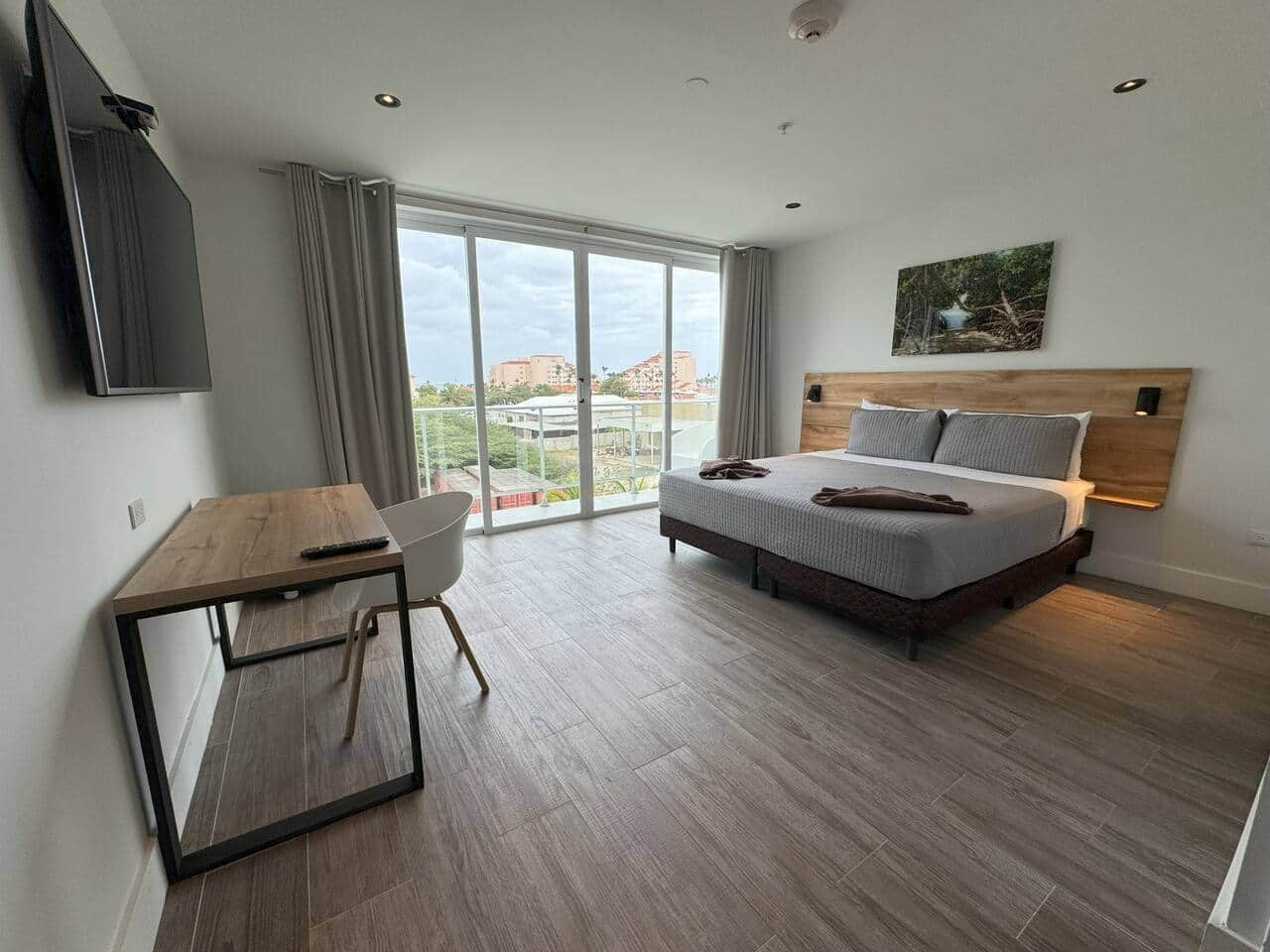 Une chambre d’hôtel moderne équipée d’un lit, d’un bureau, d’une chaise et d’une grande fenêtre donnant sur des immeubles.