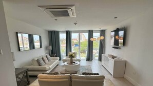 A modern living room with a sofa, a coffee table, and a TV. - 3-Suite Condo Steps to Palm Beach (Noord)