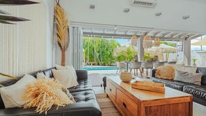 Una sala de estar moderna con un sofá de cuero negro, una mesa de centro de madera y vistas a una piscina y vegetación exterior.