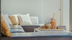 Una sala de estar moderna con un sofá, cojines, una bandeja con objetos decorativos y una ventana con persianas.