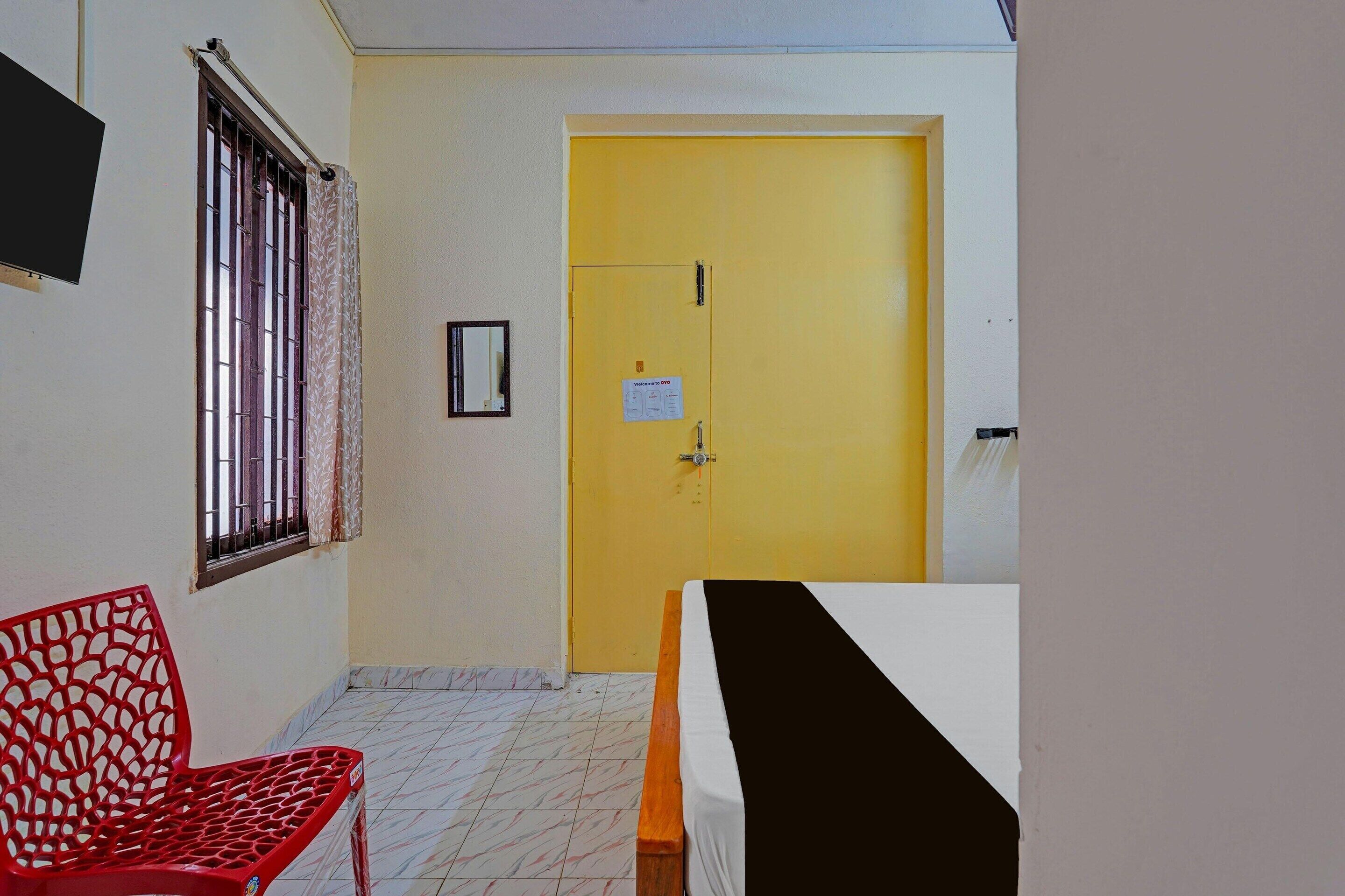 Quarto com uma cama, uma cadeira vermelha, janela com grades e uma porta amarela.