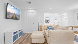 A modern living room with a large flat-screen TV, a beige sofa, a wooden bench, and a small white cabinet with wicker baskets. - Newly Renovated 3br 2ba Rancher w Patio & Parking (Ventnor City)