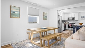 A modern kitchen with white cabinets, stainless steel appliances, and a wooden dining table with benches. - Newly Renovated 3br 2ba Rancher w Patio & Parking (Ventnor City)