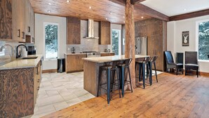 Una cocina moderna con vigas de madera, una isla central con taburetes de bar y un amplio ventanal con vistas al exterior.