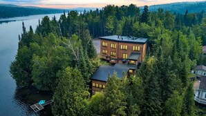 Una casa moderna rodeada de un bosque frondoso, con un muelle que se adentra en un lago.