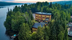 Una casa moderna rodeada de un bosque frondoso, con un muelle que se adentra en un lago.